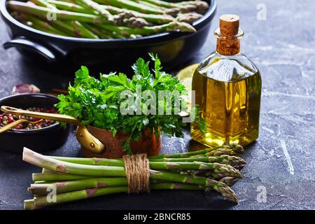 Nahaufnahme eines Strauchbundes frischen grünen Spargel mit schwarzer Backform, Flasche Olivenöl im Hintergrund, horizontale Ansicht von oben Stockfoto