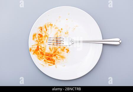 Draufsicht auf weißen Teller und Gabel, schmutziges Gericht mit Speiseresten auf grauem Hintergrund, Konzeptbild. Stockfoto