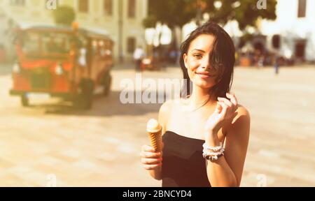 Schönes Mädchen mit Gelato lächelnd auf sonnigen Straße. Junge hübsche Frau, die Spaß hat und Eis vor dem Platz im historischen Teil von Bratis isst Stockfoto