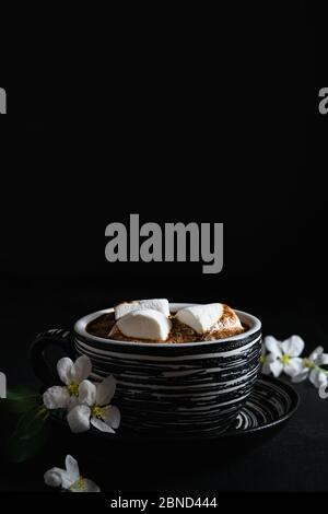 Stillleben, Tasse Kaffee mit Marshmallows und Frühlingsblumen auf schwarzem Hintergrund, leerer Platz für Text Stockfoto