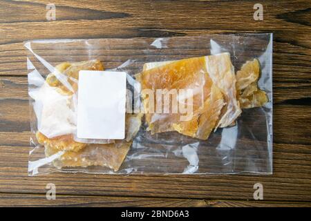 Getrocknetes Kabeljaufilet in einer transparenten Verpackung Vorspeise zu Bier auf Holzhintergrund. Snack Fisch zu Bier. Nahaufnahme Stockfoto