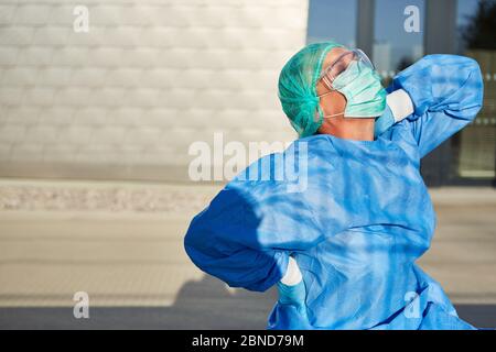 Ärztin mit Rückenschmerzen und Verspannungen vor der Klinik aufgrund von Stress und Überlastung bei der Coronavirus-Pandemie Stockfoto
