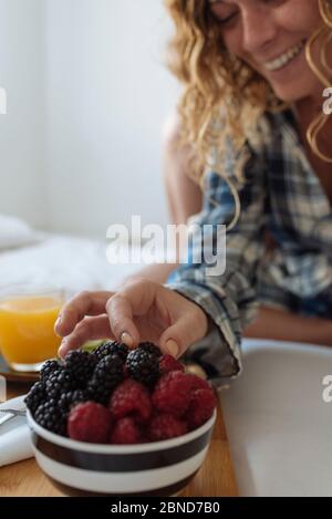 Nahaufnahme der Hand der Frau, die eine Beere von A nimmt Frühstückstablett auf dem Bett Stockfoto