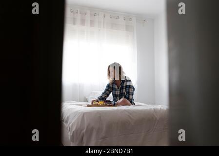 Blick durch einen Türöffler von einer Frau, die auf dem Bett gefrühstückt hat. Stockfoto