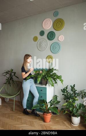 Junge Frau mit Wassersprühflasche in den Händen Pflanzen gießen Zu Hause Stockfoto