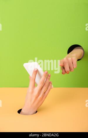Ansicht der Frau, die mit dem Finger zeigt und das Smartphone auf Grün und Orange hält Stockfoto