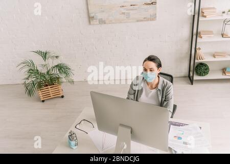 Hohe Winkelansicht des Freiberufler in der medizinischen Maske arbeiten in der Nähe Computer-Monitor zu Hause Stockfoto