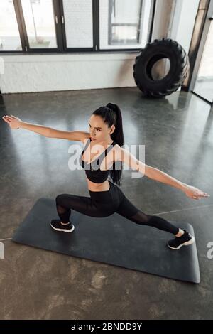 Sportlerin mit ausgestreckten Händen beim Ausfallschritt auf Fitnessmatte im Fitnessstudio Stockfoto