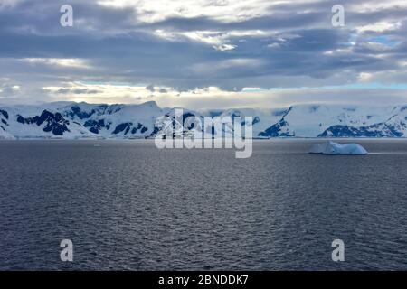 Blauer Eisberg, der an einem bewölkten Tag auf einem ruhigen Meer vor der schneebedeckten Elephant Island, Antarktis schwimmt. Von einem Kreuzfahrtschiff genommen. Stockfoto