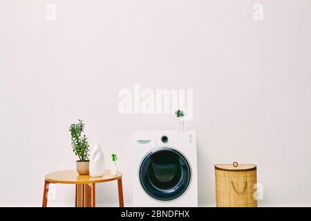 Grüne Pflanzen und Flaschen in der Nähe von Holz Couchtisch, Wäschekorb und moderne Waschmaschine im Badezimmer Stockfoto