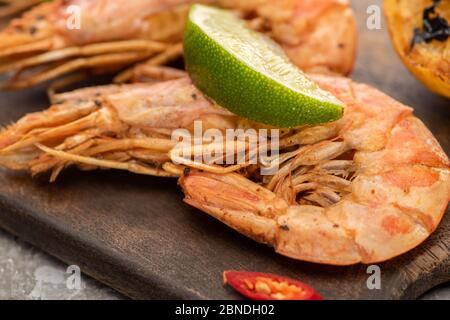 Nahaufnahme von gebratenen Garnelen mit Chili und Limette auf Holzbrett Stockfoto