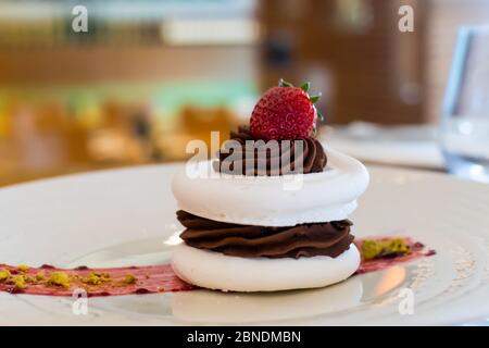 Baiser-Kuchen mit dunkler Schokolade und Erdbeere auf der Oberseite, in arestaurant-Umgebung, mit verschwommenem Hintergrund Stockfoto