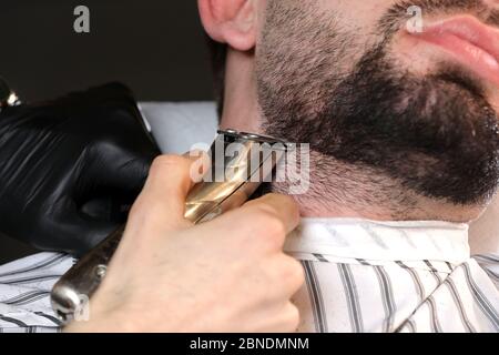 Haarschnitt eines Männerbarts in einem Friseurladen. Professioneller Meister-Barbier rasiert den Bart des Kunden mit einem elektrischen Trimmer. Barbier Men. Werbung und Stockfoto