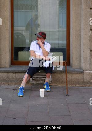 Krakau. Krakau. Polen. Älterer maskierter Mann sitzt und bettelt um Geld. Stockfoto