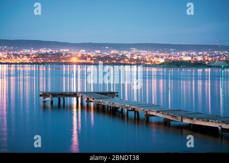 Leerer Angelpier bei Nacht mit der Stadt im Hintergrund mit Orange und blauem Grün Stockfoto