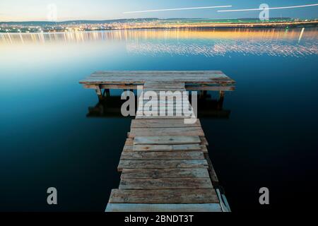Leerer Angelpier bei Nacht mit der Stadt im Hintergrund mit Orange und blauem Grün Stockfoto