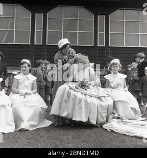 1950er, historisch, Farnworth, Greater Manchester, auf dem Gras vor einem hölzernen Sportpavillion, eine Dame mit einem Kamm in der Hand Befestigung der Krone auf dem Kopf der "Rose Queen", ein junges Mädchen im Teenageralter sitzt in einem Kleid, die die traditionelle Frühjahrsprozession führen wird. Eine Parade, die als "Walking Day" bekannt war, war im Nordwesten Englands üblich, wo sie eine jährliche Veranstaltung waren, einige aus den 1830er Jahren und viele werden noch heute abgehalten. Stockfoto