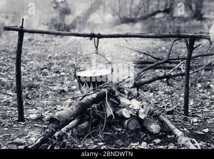 Kochen in alten rußigen Kessel am Lagerfeuer im Wald. Schwarz-Weiß-Retro-Farbbild. Stockfoto