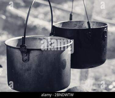 Kochen in zwei rußigen alten Kessel am Lagerfeuer an sonnigen Tag. Nahaufnahme. Schwarz-Weiß-Retro-Farbbild. Stockfoto