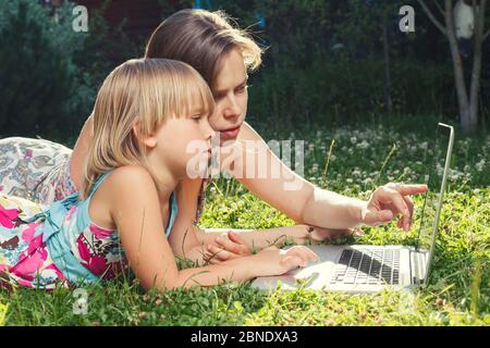 Mutter hilft ihrer kleinen Tochter, Laptop-Computer zu verwenden. Kind zu Hause lernen, ihre Hausaufgaben oder Online-Unterricht. Homeschooling Konzept Stockfoto