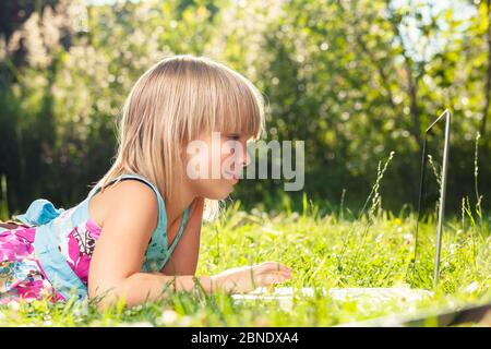 Kleines Mädchen mit Laptop-Computer in einem Hinterhof. Kind zu Hause lernen, ihre Hausaufgaben oder Online-Unterricht. Homeschooling Konzept Stockfoto