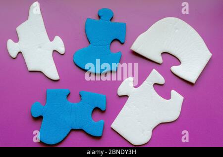 Fragmente des Puzzles auf einem fliederfarbenen Hintergrund. Weiße und blaue unmontierte Rätsel. Psychologische Gesundheit und logisches Denken. Blick von oben. Stockfoto