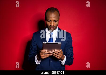 Porträt von seinem er schön attraktive Inhalte konzentriert Kerl Investor Entwickler hält in Händen ebook Lesen Börse Nachrichten isoliert über rot kastanienbraun Stockfoto