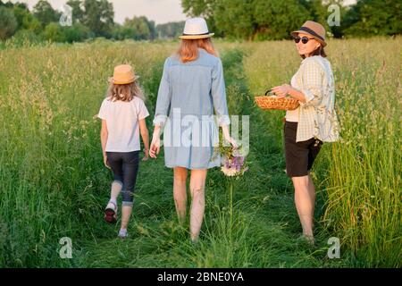 Mutter und Kinder zwei Töchter, die auf einer Landstraße durch die Wiese laufen Stockfoto