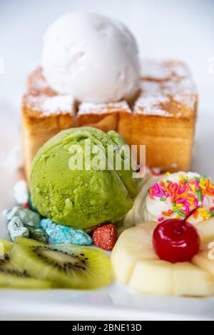 Closeup Honig Toast Brot serviert mit grünem Tee und Kokosmilch Eiskugel, dekorieren mit Kirsche, Apfel, Kiwi-Obst und Sahne Zucker Topping spr Stockfoto