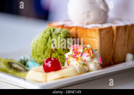 Closeup Honig Toast Brot serviert mit grünem Tee und Kokosmilch Eiskugel, dekorieren mit Kirsche, Apfel, Kiwi-Obst und Sahne Zucker Topping spr Stockfoto