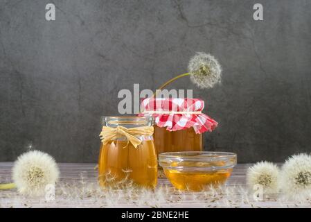 Löwenzahn-Marmelade, Honig, Gelee in einem Glasgefäß auf einem Holztisch, schwarzer Hintergrund mit frischen Blumen, Löwenzahn luftigen Samenköpfen, Samen, Blaskugeln Stockfoto
