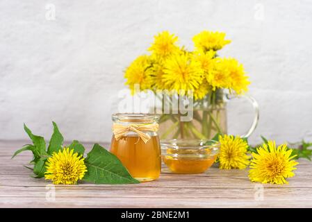 Löwenzahn-Marmelade, Honig, Gelee in einem Glasgefäß auf einem Holztisch, weißer Hintergrund mit frischen gelben Löwenzahn-Blüten. Medizin, gesunde Ernährung, Gesundheit Stockfoto