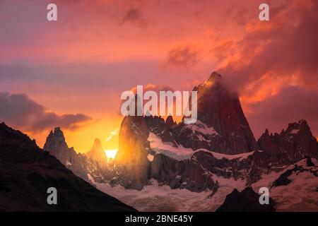 Felsige schneebedeckte Berggipfel mit der Sonne hinter sich und roten Wolken. Fritz Rroy in Argentinien Stockfoto