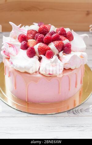 Rosa Käsekuchen mit geschmolzener Schokolade, Baiser, frischen Himbeeren und Erdbeeren. Holzhintergrund. Stockfoto