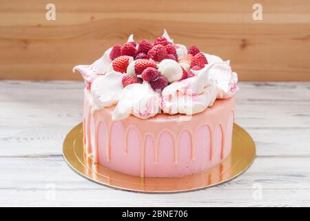 Rosa Käsekuchen mit geschmolzener Schokolade, Baiser, frischen Himbeeren und Erdbeeren. Holzhintergrund. Stockfoto