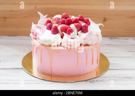 Rosa Käsekuchen mit geschmolzener Schokolade, Baiser, frischen Himbeeren und Erdbeeren. Holzhintergrund. Stockfoto