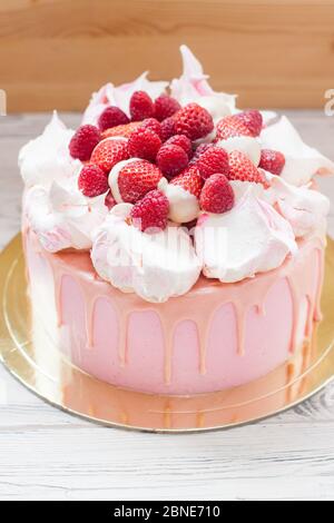 Rosa Käsekuchen mit geschmolzener Schokolade, Baiser, frischen Himbeeren und Erdbeeren. Holzhintergrund. Stockfoto