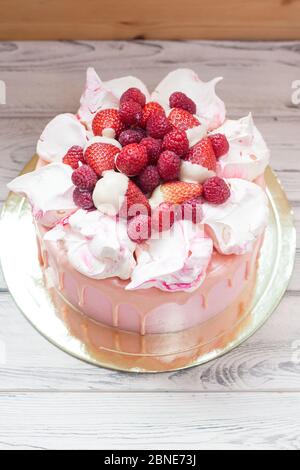 Rosa Käsekuchen mit geschmolzener Schokolade, Baiser, frischen Himbeeren und Erdbeeren. Holzhintergrund. Stockfoto