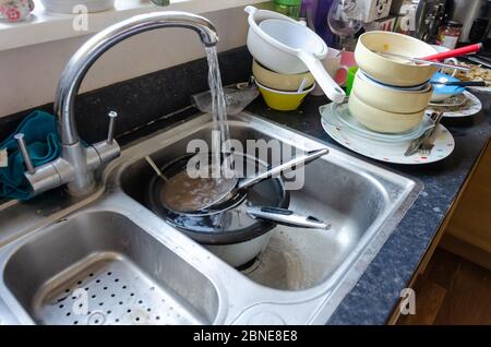 Fließendes Wasser aus einem Wasserhahn füllt Kochtöpfe, die in einem Spülbecken einweichen. Das Geschirr wird zum Spülen gestapelt. Stockfoto