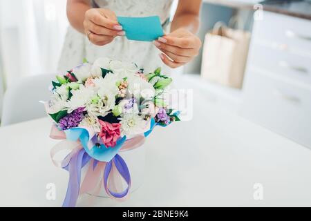 Frau liest Karte in Blumenstrauß von Freund in Geschenkbox auf der Küche zu Hause gelassen. Überraschungsgeschenk Stockfoto