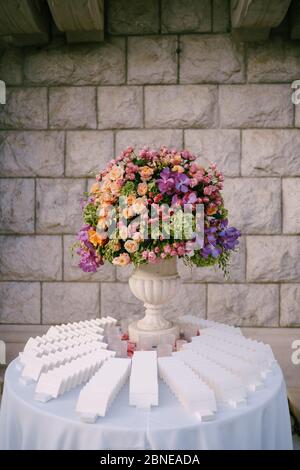 Empfang am Tisch für Hochzeitsessen. Ein riesiger Strauß in einer alten Marmorvase aus rosa, roten, orangen und gelben Rosen, grünen Hortensien, lila Orchideen. Standfüße Stockfoto