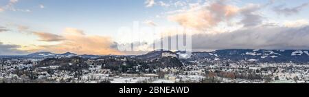 Panorama-Luftdrohne Blick auf den Salzburger Berg und verschneiten Rand mit Blick auf die Festung Hohensalzburg bei Sonnenuntergang Stockfoto