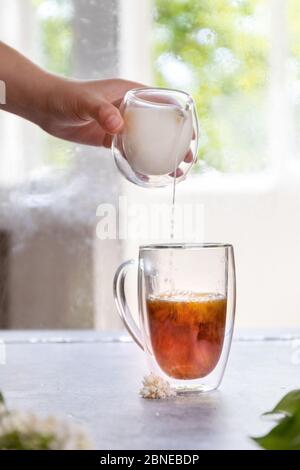 Nahaufnahme der weiblichen Hand, die Milch in Tee gießt, vertikales Foto Stockfoto