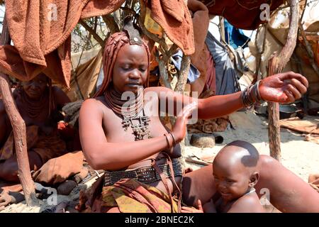 Himba Frau, die Otjize (eine Mischung aus Butter, Ocker und Asche) auf ihre Haut aufsetzt. Marienfluss Tal. Kaokoland, Namibia Oktober 2015 Stockfoto