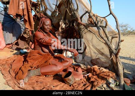 Himba Frau in ihrer temporären Hütte, die Otjize (eine Mischung aus Butter, Ocker und Asche) auf ihre Haut aufsetzt. Marienfluss Tal. Kaokoland, Namibia Oktober 2015 Stockfoto