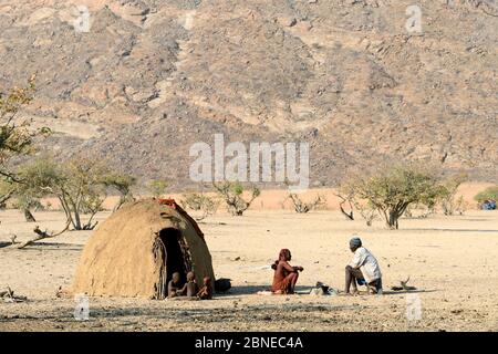 Familie Himba neben der traditionellen Schlammhütte, Marienfluss Tal während der Trockenzeit. Kaokoland, Namibia. Oktober 2015 Stockfoto