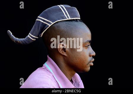 Junger Himba-Mann mit einem einzigen Zopf, der mit einem Hut bedeckt ist und anzeigt, dass er unverheiratet ist. Kaokoland, Namibia Oktober 2015 Stockfoto