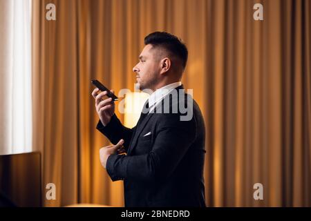 Ein junger Mann in einem Anzug, der am Telefon spricht Verwenden der Lautsprechermod Stockfoto