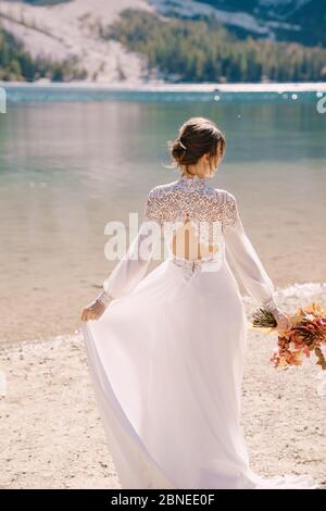 Schöne Braut in einem weißen Kleid mit Ärmeln und Spitze, mit einem gelben Herbststrauß von getrockneten Blumen und Pfingstrosen, am Lago di Prags in Italien Stockfoto