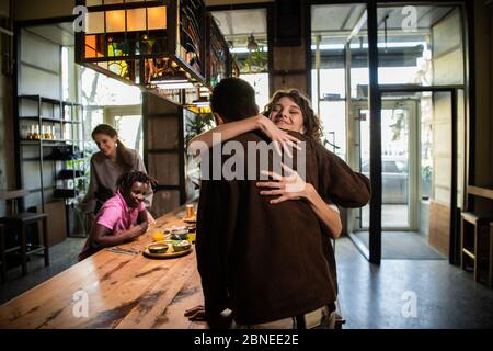 Ein junges hübsches Mädchen umarmt einen Jungen in einem Café, um ihn zu begrüßen, ihre Stockfoto